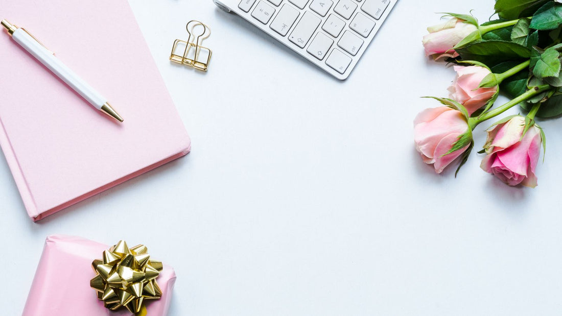A tidy office desk with a wrapped gift, pink roses, a notebook and a keyboard