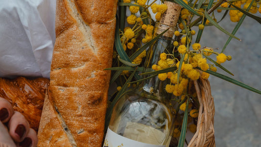 Rustic woven basket with a bottle of wine, fresh bread and yellow flowers — a hostess gift ready to give