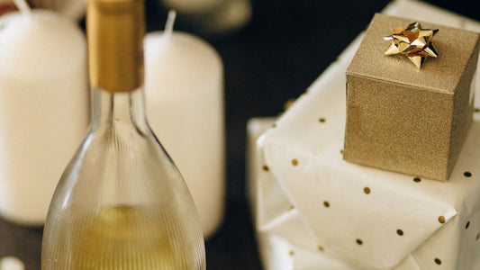 A bottle of wine resting beside wrapped gifts on a table, ready to be brought to a dinner party
