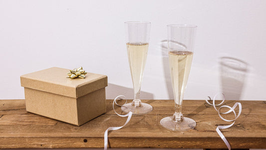 Wine, two glasses and a wrapped gift box on a warm wooden table — affordable wine gift ideas under $25