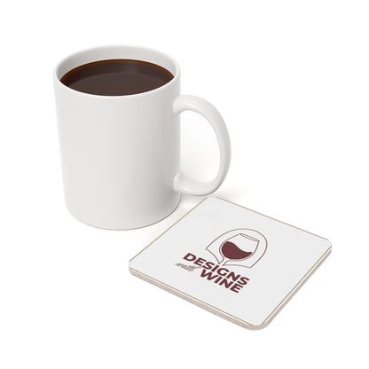 Designs With Wine logo cork-back coaster — on a table with a mug