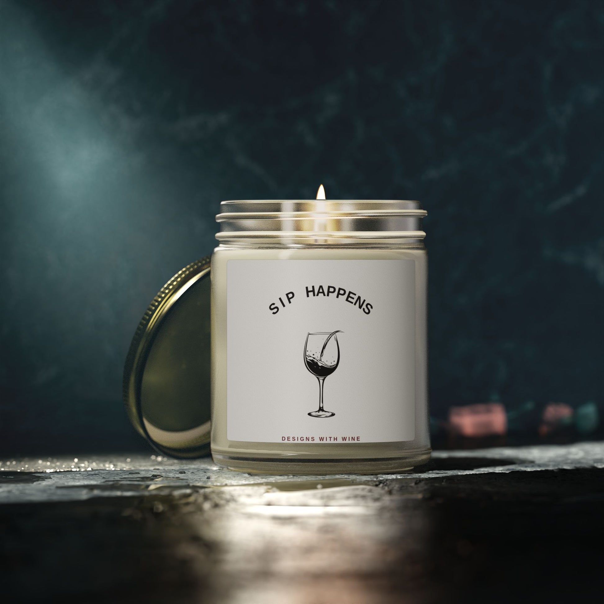 Sip Happens candle lit on a dark reflective surface against a moody teal backdrop