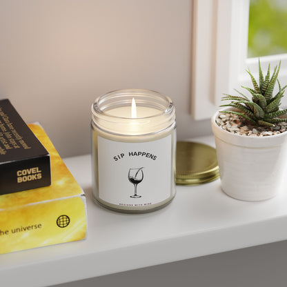 Sip Happens candle lit on a windowsill beside stacked books and a potted succulent
