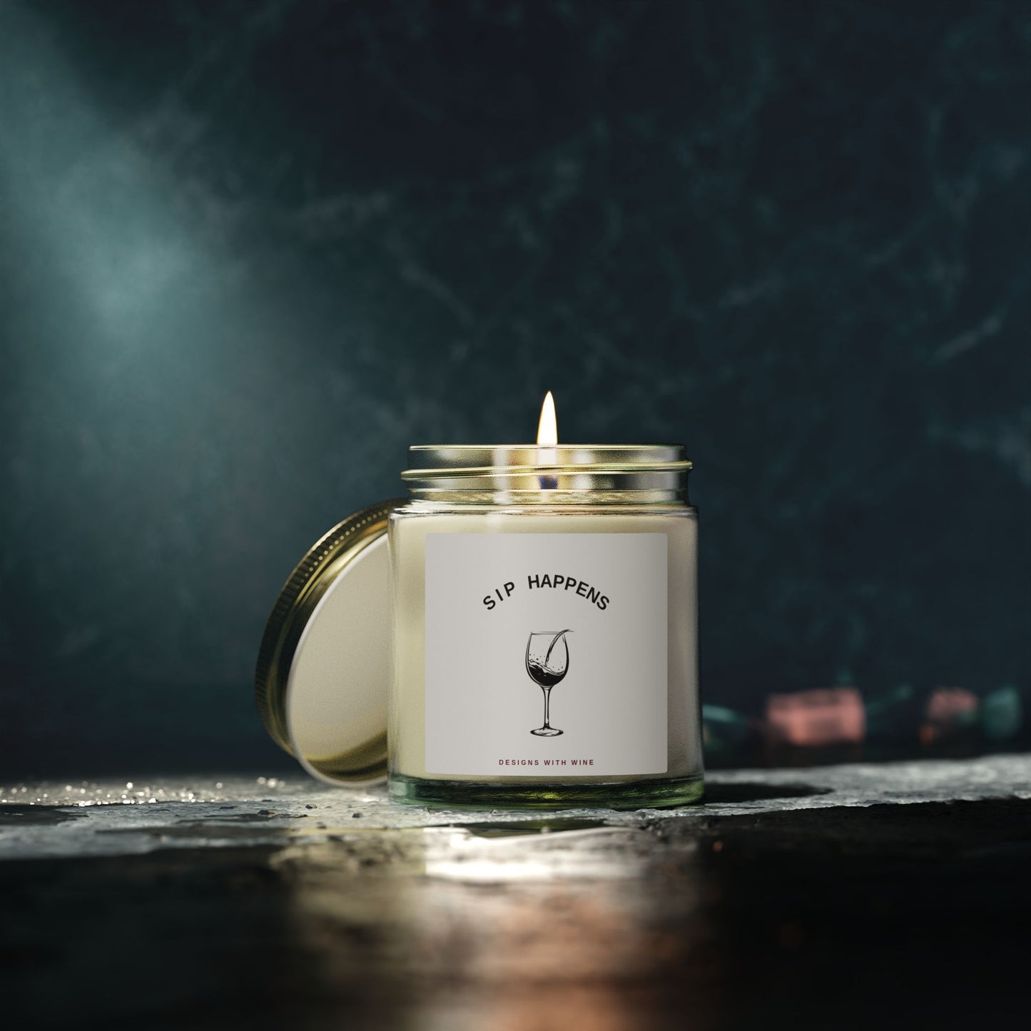 Sip Happens candle lit on a dark reflective surface against a moody teal backdrop