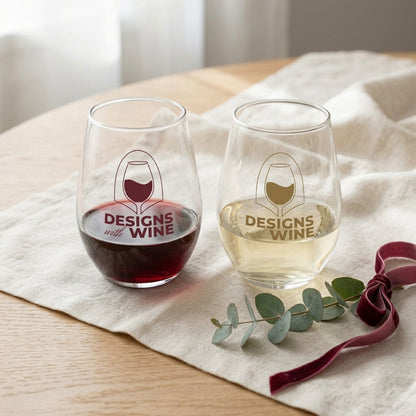 The Pair gift set styled together — Red Wine Lover and White Wine Lover stemless glasses with a pour of each, on linen with eucalyptus and a wine-red ribbon